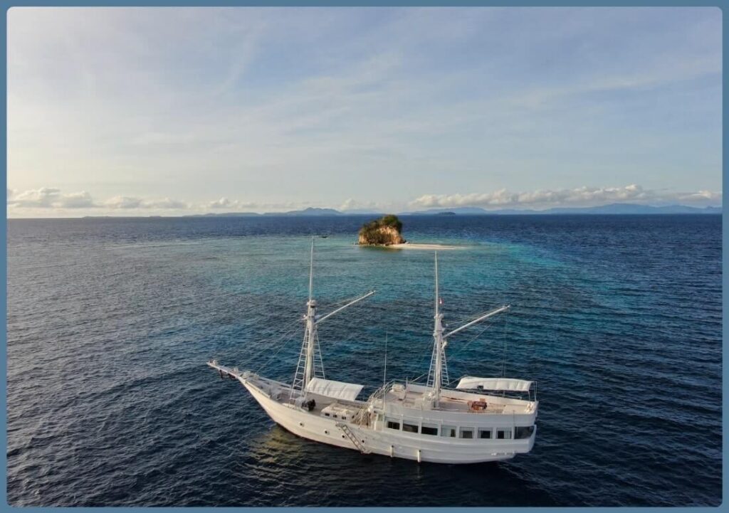  Luxury Sailing Yacht floats in the vast ocean, with a picturesque island visible in the background, creating a tranquil scene.