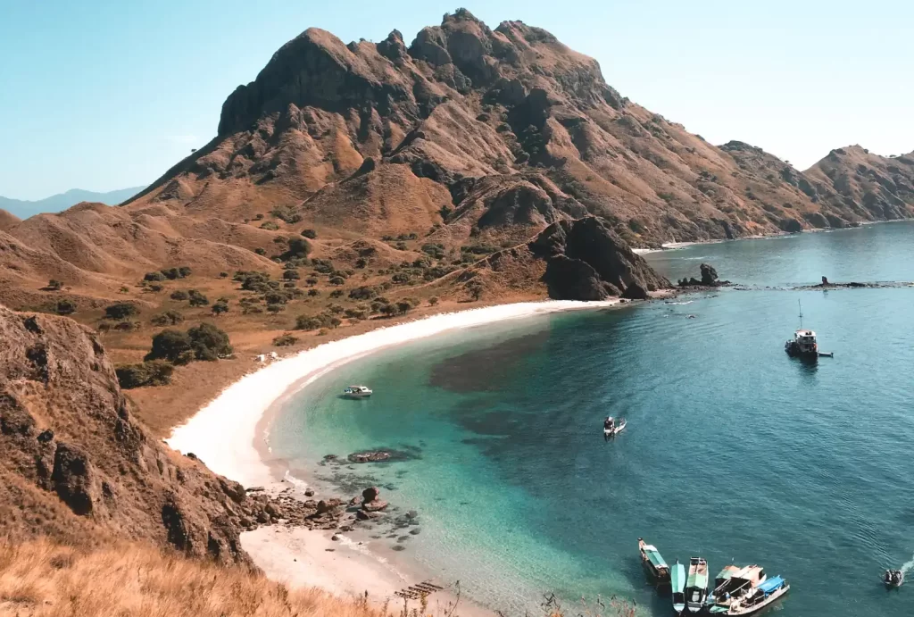 Stunning beach view from Padar Island, featuring boats and majestic mountains in the background, Labuan Bajo, Indonesia.