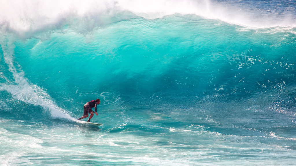 A surfer skillfully rides a massive turquoise wave, capturing the thrill and intensity of the moment. The powerful wave curls and crashes behind him, while the vibrant shades of blue and white create a dramatic contrast. Best Time to Visit the Philippines