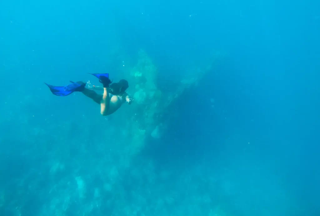 A woman dives in the ocean, exploring the Japanese shipwreck in Coron while wearing a scuba mask.