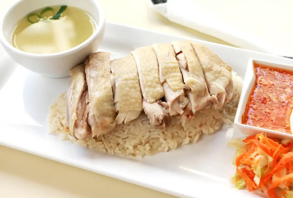 A delicious plate of Hainanese chicken and rice, drizzled with savory sauce, ready to be enjoyed.