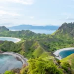 Scenic view of Padar Island in Komodo National Park, Flores, Indonesia. The image showcases the iconic green hills, crescent-shaped beaches, and turquoise waters under a clear blue sky, illustrating the island's breathtaking natural beauty.