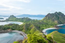 Scenic view of Padar Island in Komodo National Park, Flores, Indonesia. The image showcases the iconic green hills, crescent-shaped beaches, and turquoise waters under a clear blue sky, illustrating the island's breathtaking natural beauty.