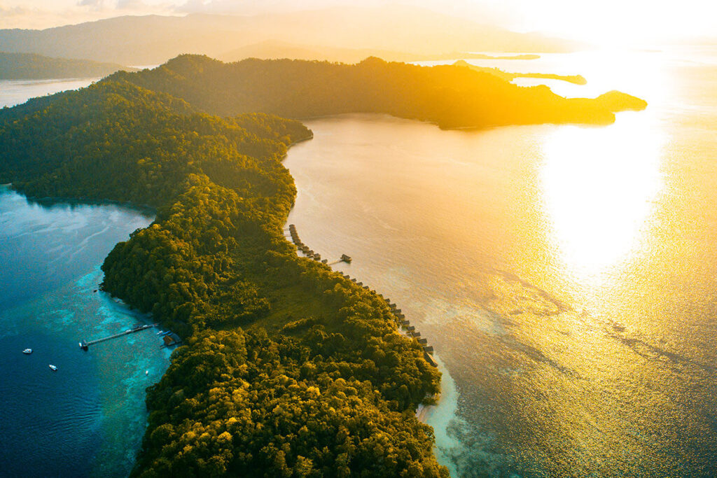 A boat glides through the ocean waters near a majestic mountain, showcasing the beauty of Raja Ampat's Eco Resort.