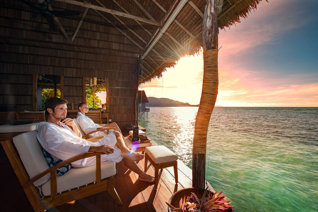 A couple enjoys a serene moment on a wooden deck, gazing at the stunning ocean view in Raja Ampat.