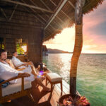 A couple enjoys a serene moment on a wooden deck, gazing at the stunning ocean view in Raja Ampat.