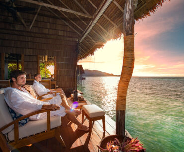 A couple enjoys a serene moment on a wooden deck, gazing at the stunning ocean view in Raja Ampat.