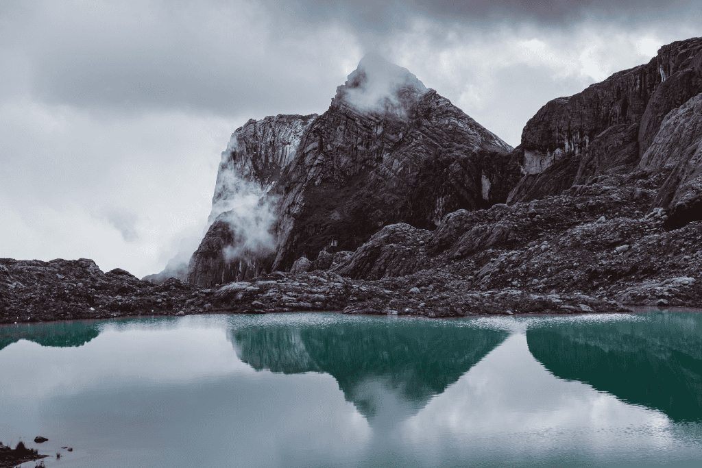 Majestic Puncak Jaya mountain towering over a serene lake, with fluffy clouds beautifully mirrored on the water's surface.