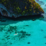 "Two travelers enjoying water activities in the crystal-clear turquoise waters of Raja Ampat, surrounded by lush limestone cliffs and vibrant coral reefs, showcasing the natural beauty of this Indonesian paradise."