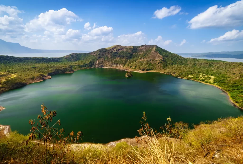 A stunning view of Taal volcano crater, featuring a large lake embraced by majestic mountains and lush grass.