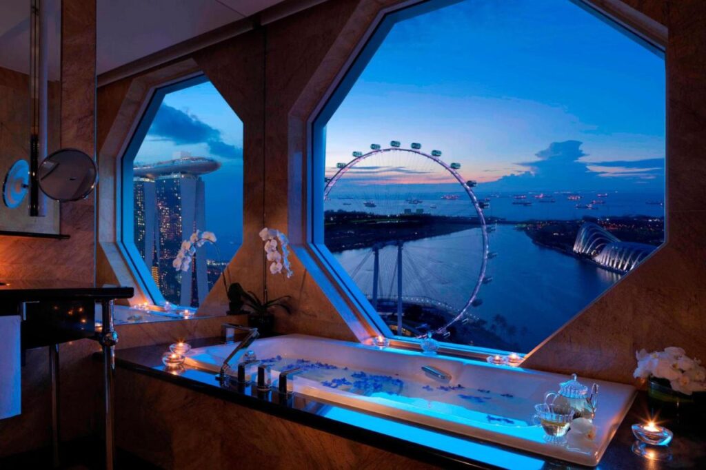 Luxurious bathroom at The Ritz-Carlton, Millenia Singapore, featuring a stunning city view and a ferris wheel in the distance.