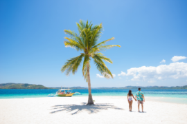 Couple on a tropical beach with blue water and palm tree ( Coron, Philippines)