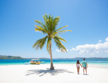 Couple on a tropical beach with blue water and palm tree ( Coron, Philippines)