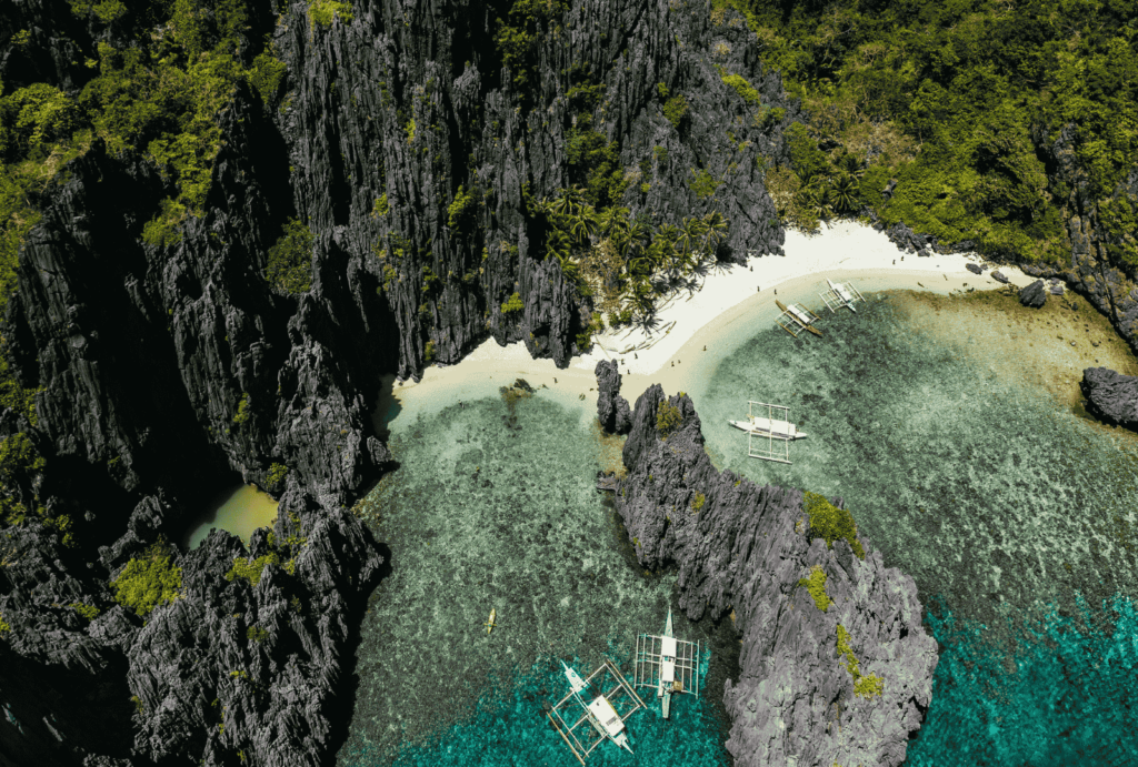 Aerial view -blue lagoon in El Nido. people walking in white sand beach with background of jungle. boats at the beach 