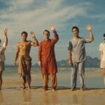 5. People standing on the beach, waving their hands in excitement, enjoying a sunny day by the ocean.