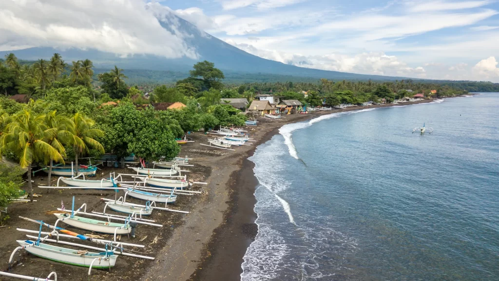 Traditional jukung outrigger fishing boats on the black volcanic sand of Amed Beach, eastern Bali, with Mount Agung rising behind — a working fishing village and world-class dive destination on Bali's unspoiled east coast