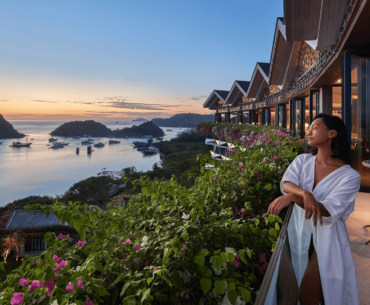 A woman stands on a hotel balcony at a resort, gazing out at the beautiful ocean, soaking in the tranquil surroundings.