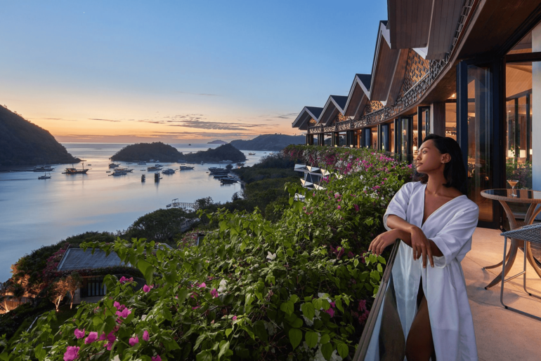 A woman stands on a hotel balcony at a resort, gazing out at the beautiful ocean, soaking in the tranquil surroundings.