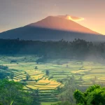 Sunrise over terraced rice fields beneath Mount Agung, Bali's sacred volcano, viewed from the quiet eastern highlands — the Bali that exists beyond Seminyak and Ubud's well-worn trails