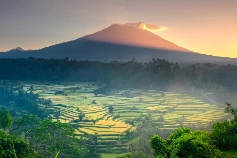 Sunrise over terraced rice fields beneath Mount Agung, Bali's sacred volcano, viewed from the quiet eastern highlands — the Bali that exists beyond Seminyak and Ubud's well-worn trails