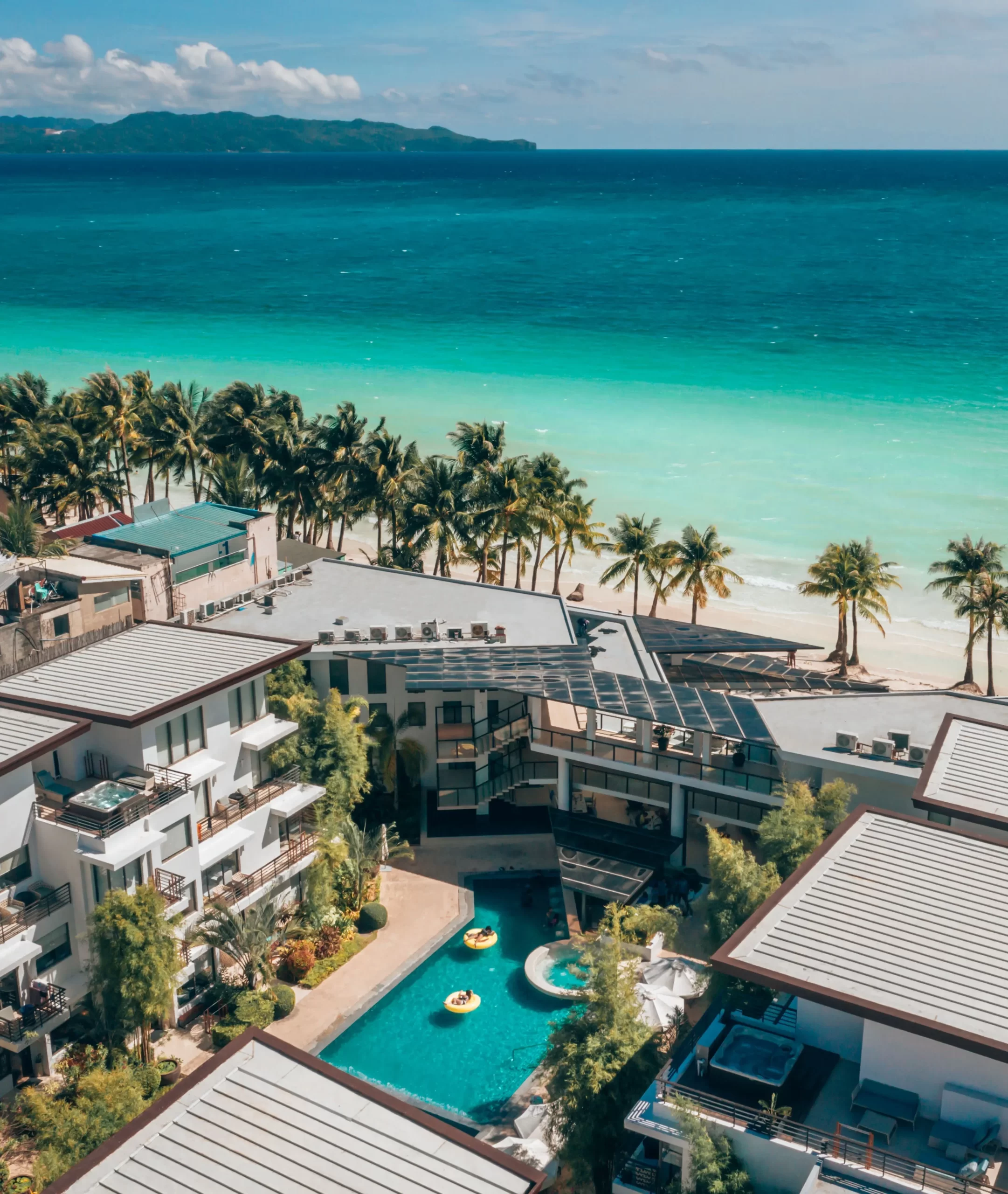 Aerial view of a luxury beachfront resort with a swimming pool, palm trees, and turquoise ocean in Boracay, Philippines.