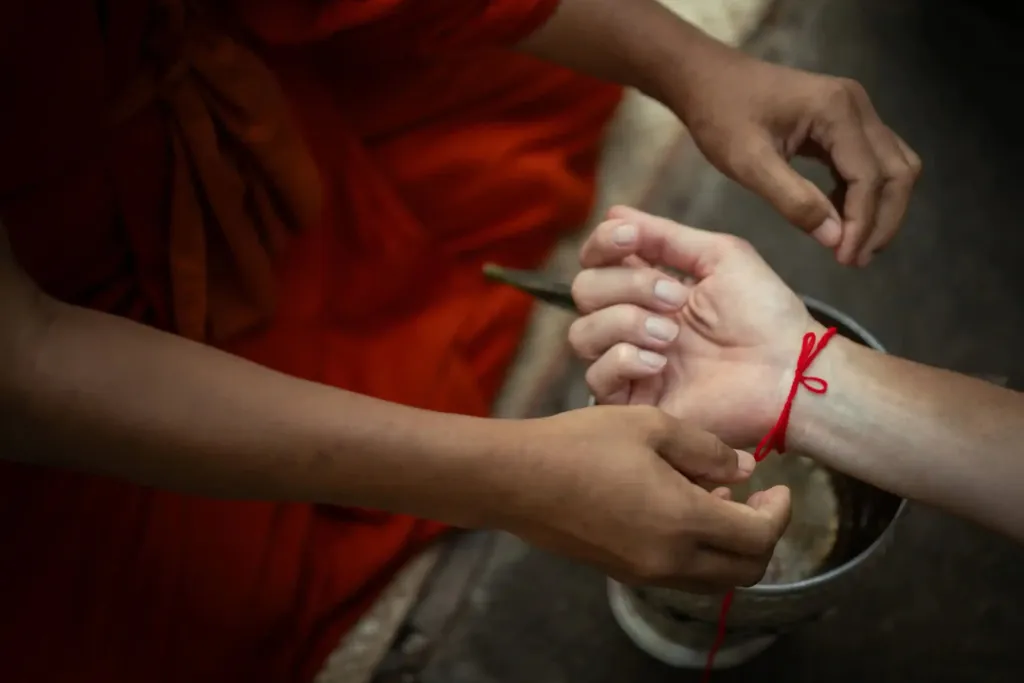 Buddhist monk tying a red blessing string on a traveller's wrist during a private temple ceremony