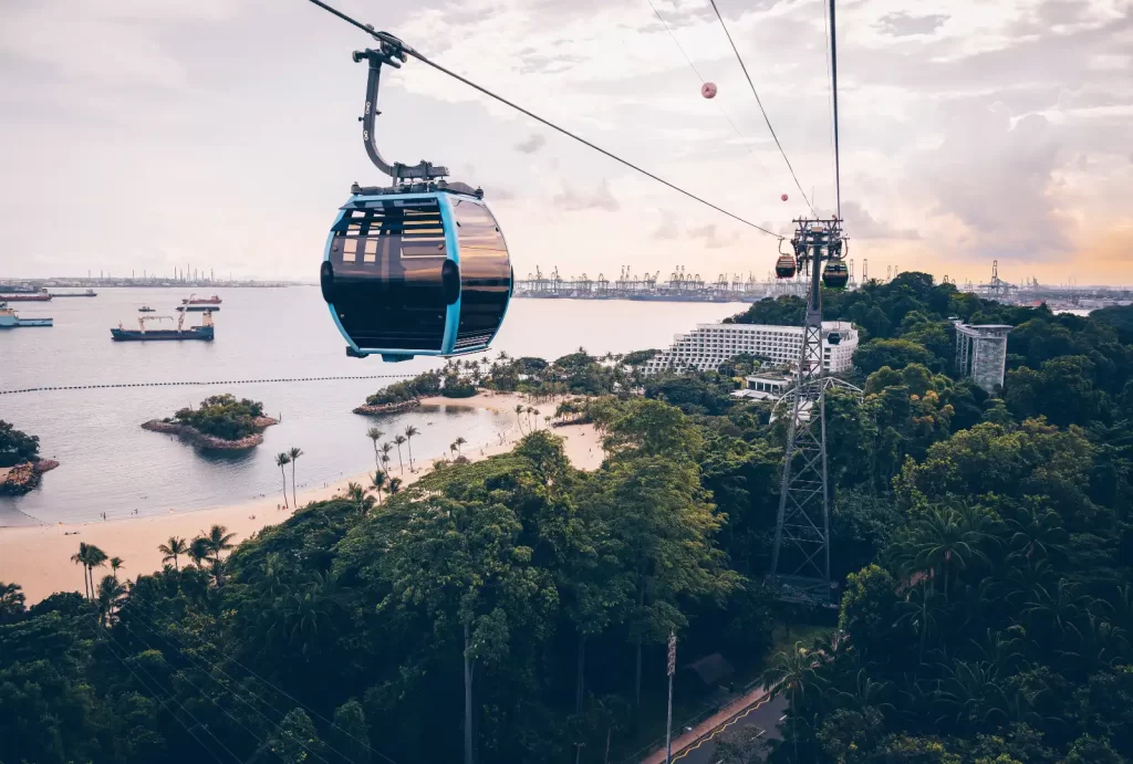 A scenic cable car glides over water, showcasing a boat below, set against the beautiful backdrop of Sentosa Island, Singapore.