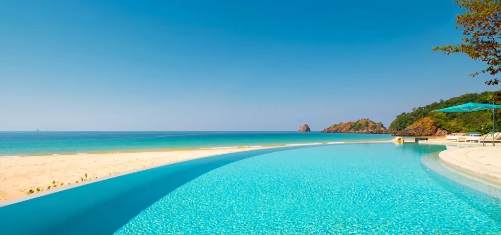 Luxury beachfront infinity pool overlooking a pristine white sand beach and turquoise sea with a rocky island headland in the background — Discovery DMC