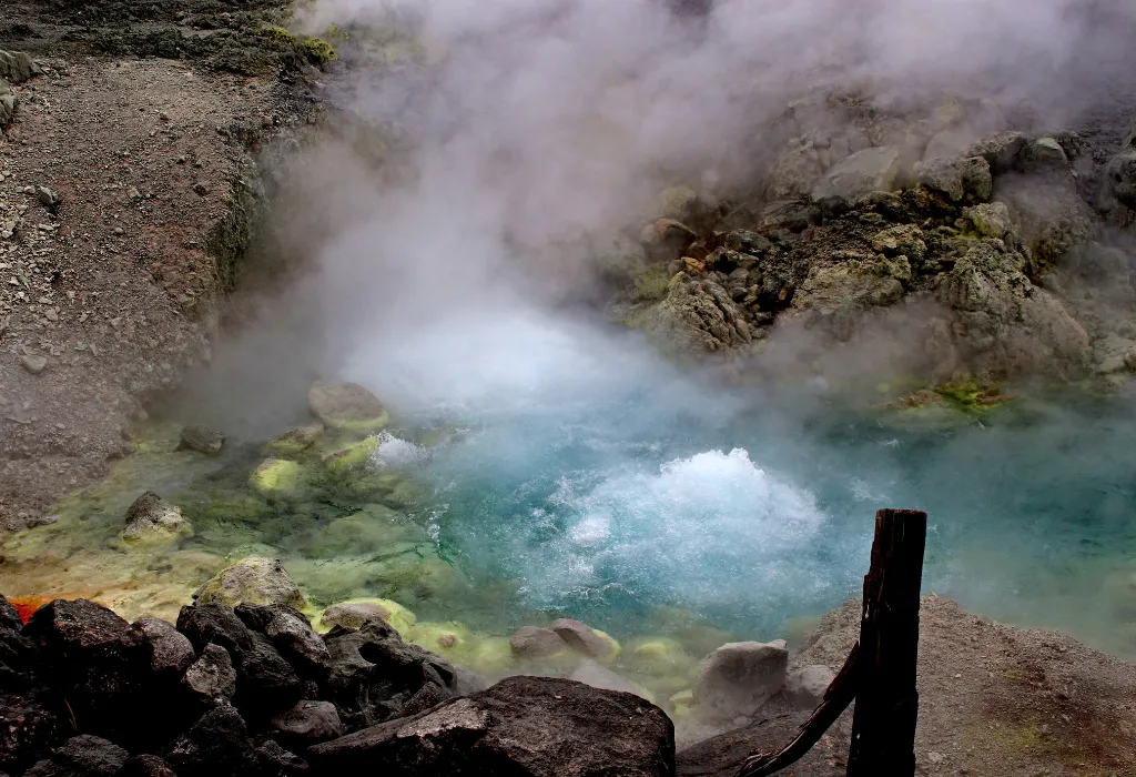Steaming, colorful geothermal pool showcasing a natural Onsen hot spring source in a volcanic landscape. Experience Japan's raw beauty and unique luxury wellness on custom Japan travel itineraries with a Japan dmc.