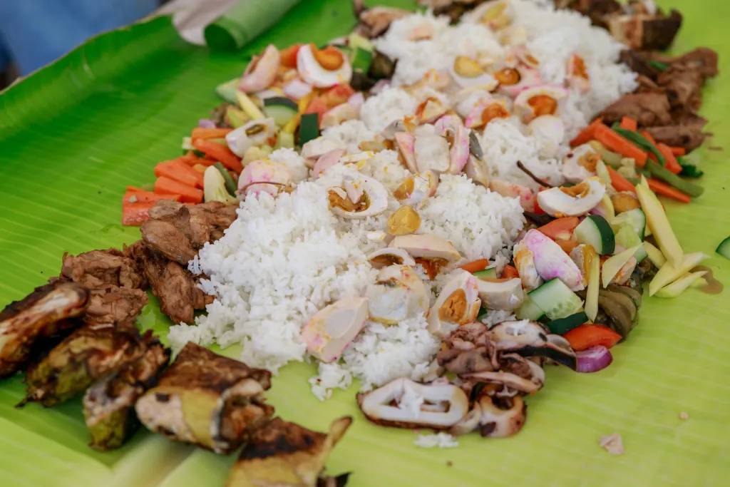 Filipino kamayan feast of rice, grilled meats, salted eggs and seafood on banana leaves
