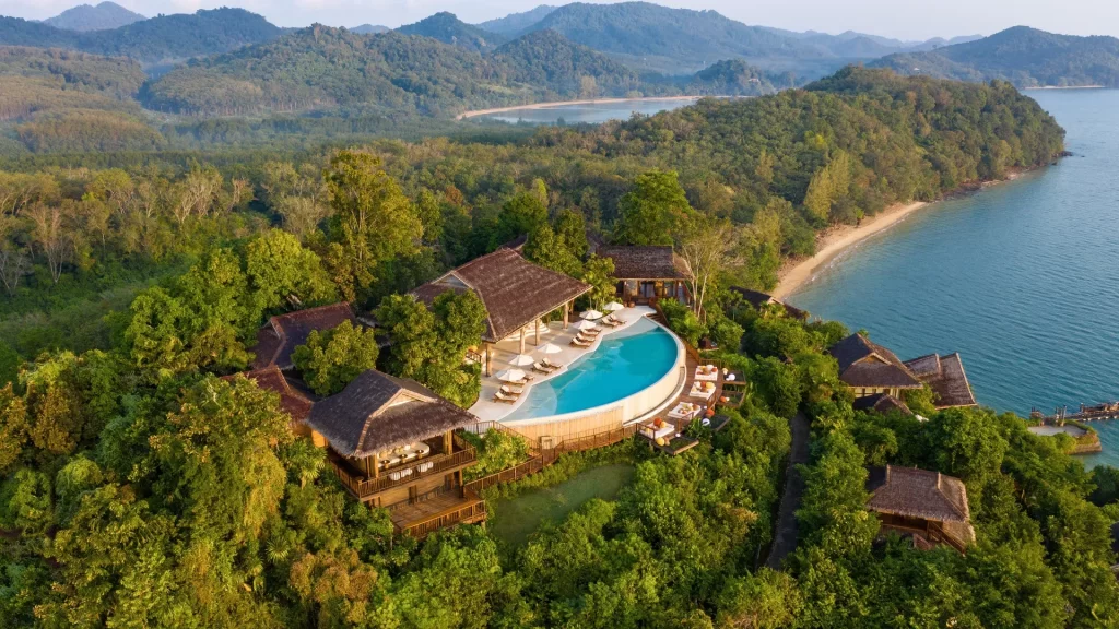 erial view of a hilltop luxury resort in Thailand with a stunning infinity pool overlooking tropical jungle, mountains, and a private beachfront — luxury Thailand DMC experience