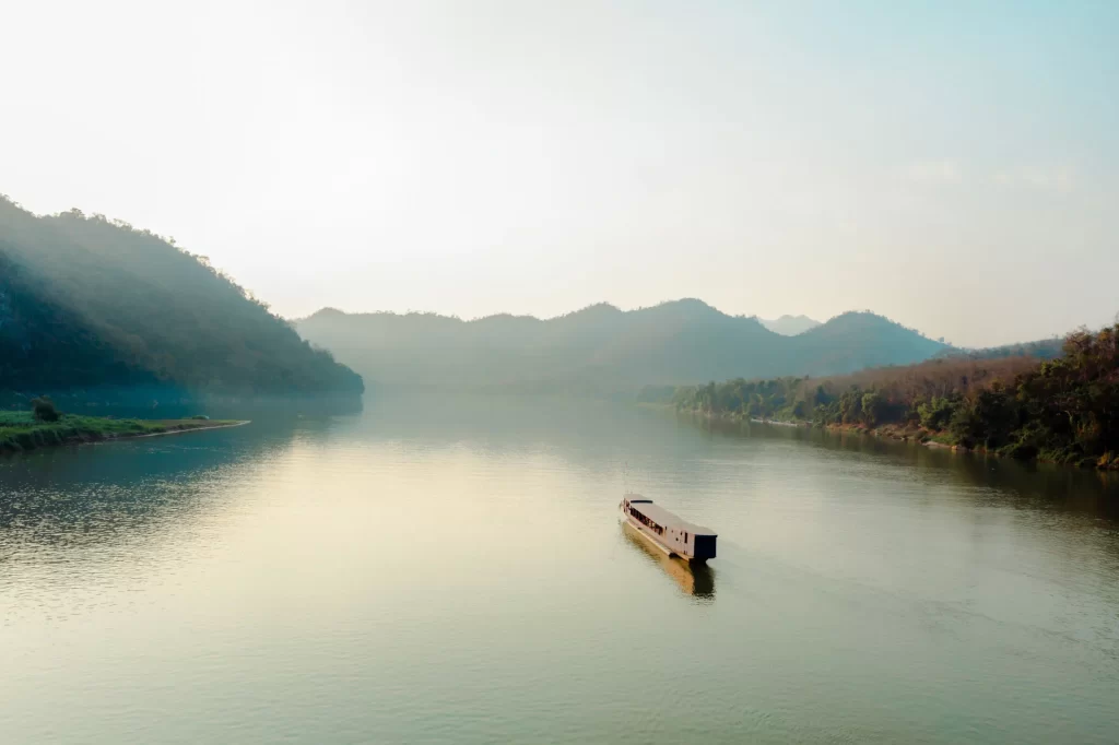 Private river cruise boat on the Mekong River at sunrise, with misty forested hills in northern Laos