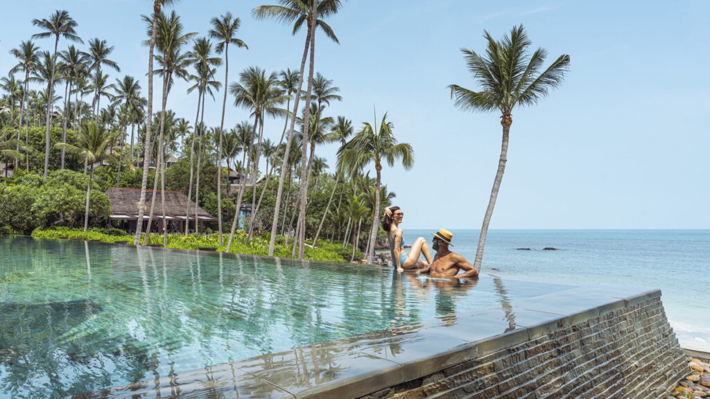 A couple relaxes on the edge of an infinity pool at Four Seasons Resort Koh Samui, enjoying stunning views.