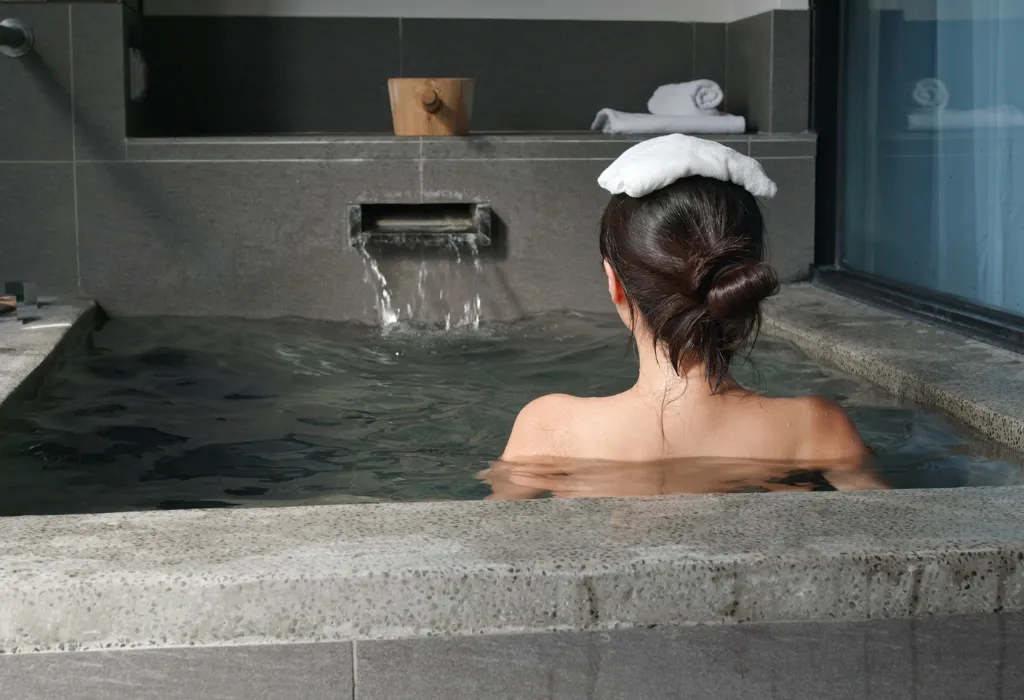 Woman relaxing in a private, modern onsen bath with a cold towel on her head. Experience this exclusive relaxation on your custom luxury Japan tours and Japan holidays.