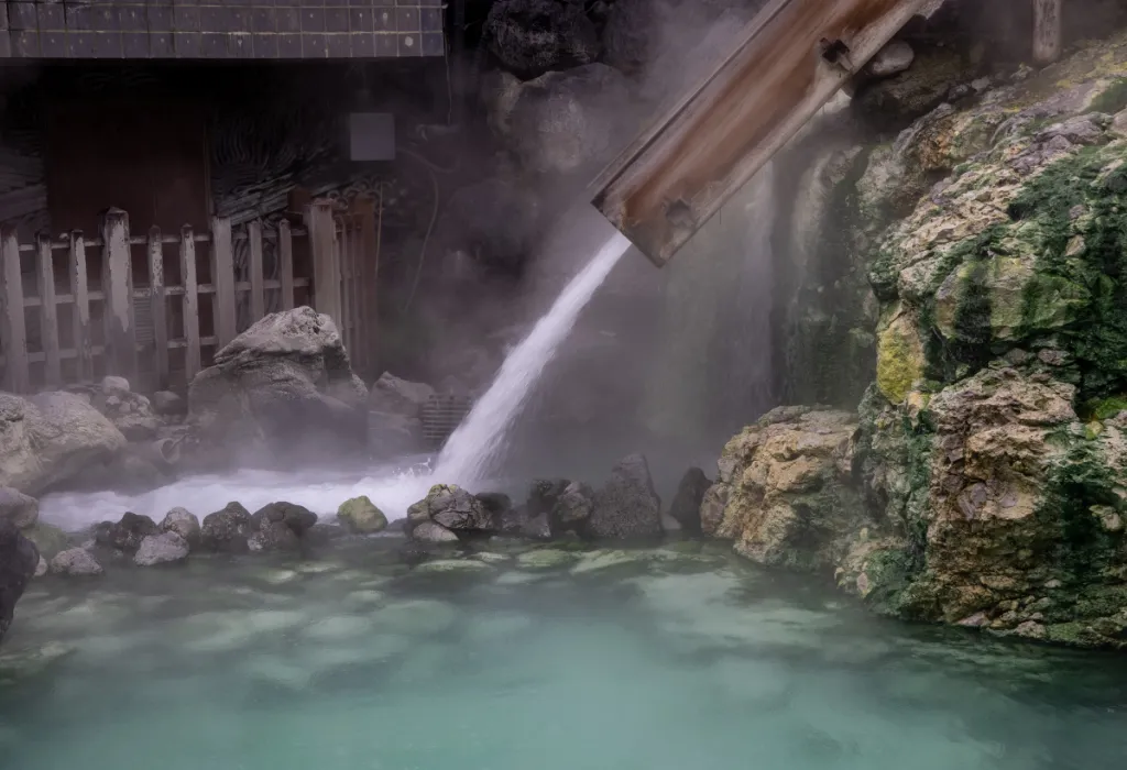 Steaming luxury outdoor onsen (hot spring) bath in Japan with turquoise water and natural rock, perfect for a relaxing Japan tour or Japan holiday.