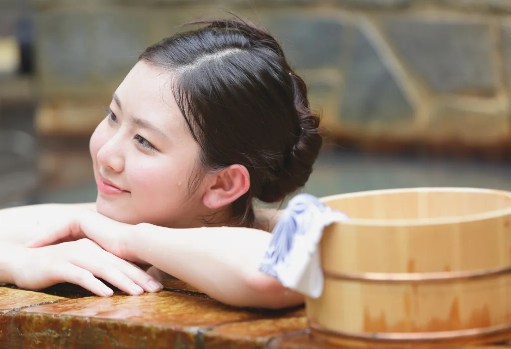 Beautiful woman relaxing in a traditional Japanese onsen bath, showcasing the ultimate relaxation experience on a luxury Japan tour.