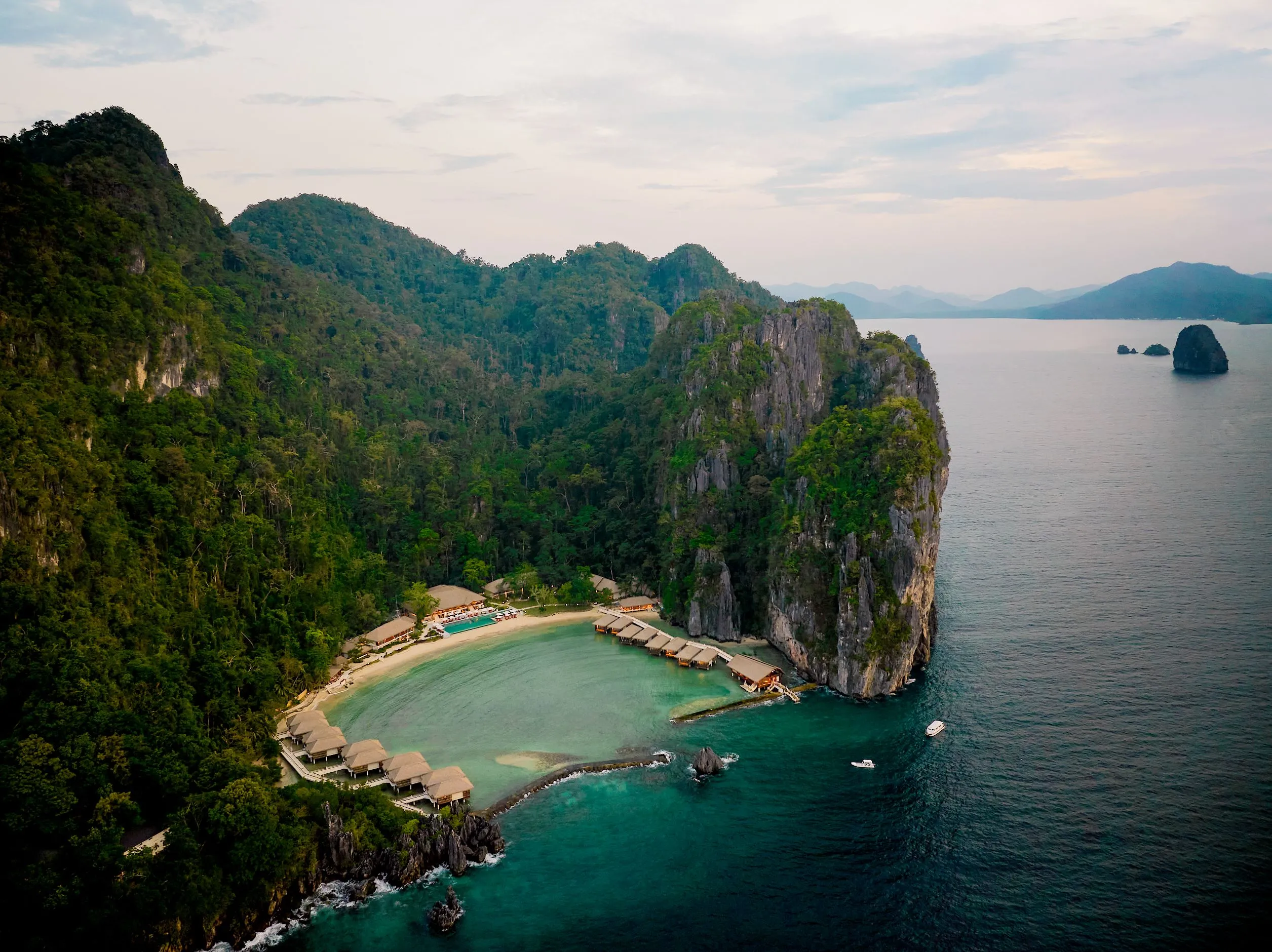 Aerial view of luxury water cottages and beach villas nestled between limestone cliffs and a turquoise lagoon in El Nido, Palawan.