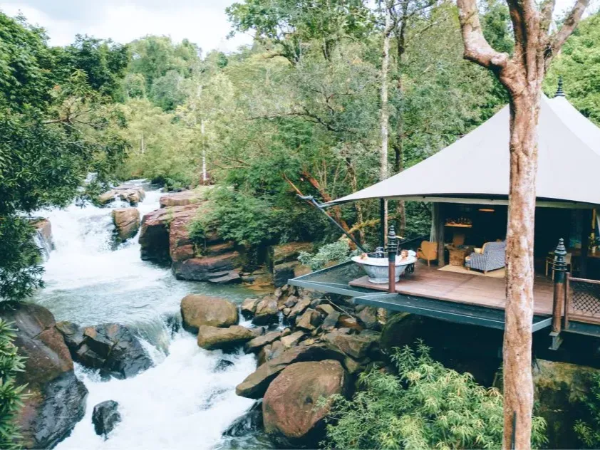 A luxury safari-style tent with a private outdoor bathtub overlooking a cascading waterfall in the Cambodian jungle, representing world-class eco-tourism by a premier Cambodia DMC.