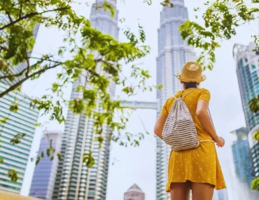 A traveler in a sunhat looks up at the iconic Petronas Twin Towers in Kuala Lumpur, the perfect destination for your next Malaysia holiday.
