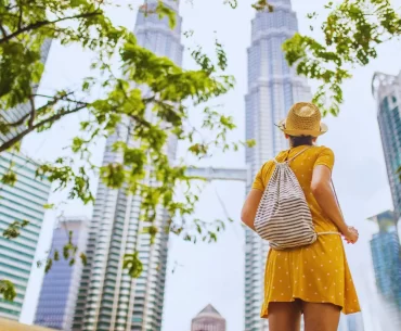 A traveler in a sunhat looks up at the iconic Petronas Twin Towers in Kuala Lumpur, the perfect destination for your next Malaysia holiday.