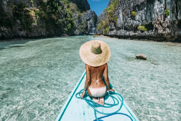 A luxury traveler on a private traditional boat entering Big Lagoon, El Nido. Tailored Palawan island hopping itineraries provided by a leading Philippines DMC.