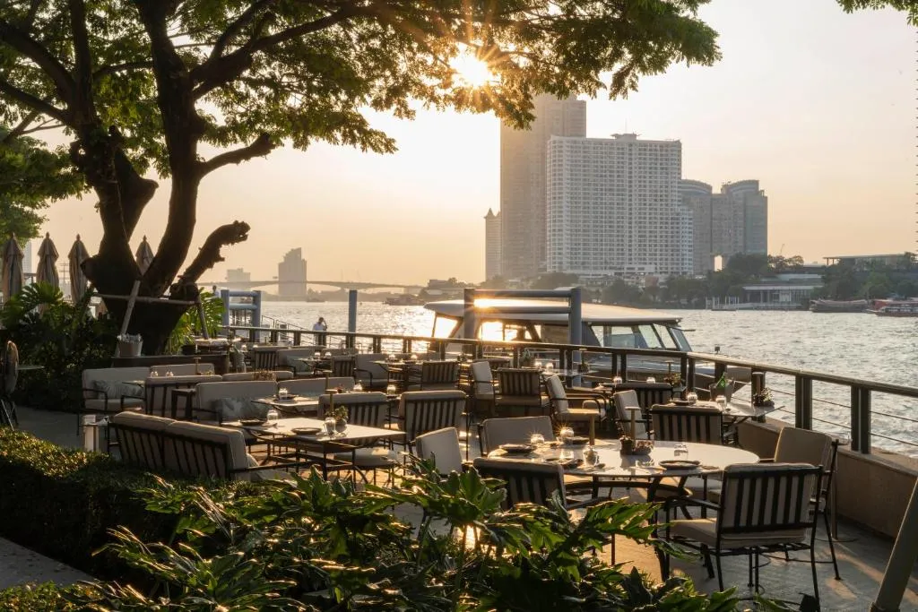 Elegant outdoor riverside restaurant at sunset along the Chao Phraya River in Bangkok, with golden light and city skyline views — luxury Thailand travel by a top Thailand DMC and tour operator