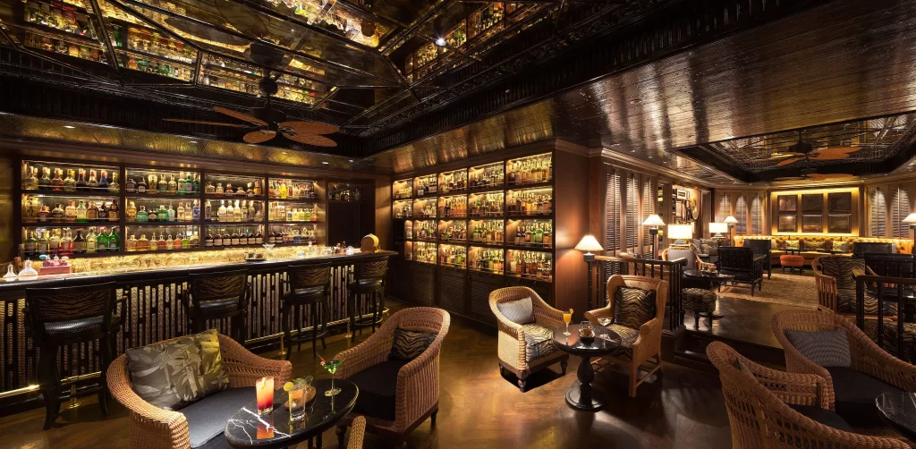 The Bamboo Bar at Mandarin Oriental Bangkok — a legendary colonial-era cocktail lounge with rattan armchairs, ceiling fans, and floor-to-ceiling shelves of spirits, one of Asia's great hotel bars