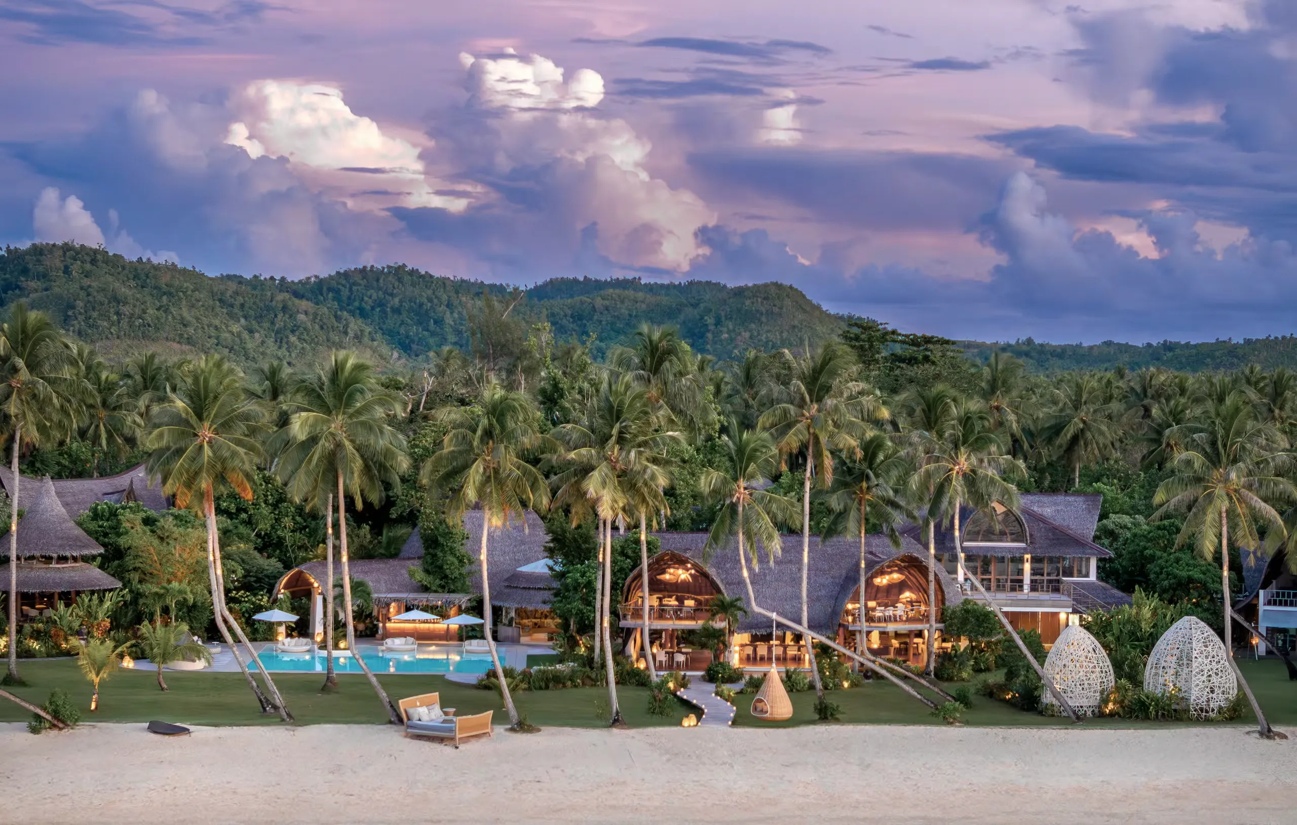 Nay Palad Hideaway, a luxury villa resort in Siargao, Philippines, with thatched villas, an infinity pool, and palm trees at sunset.