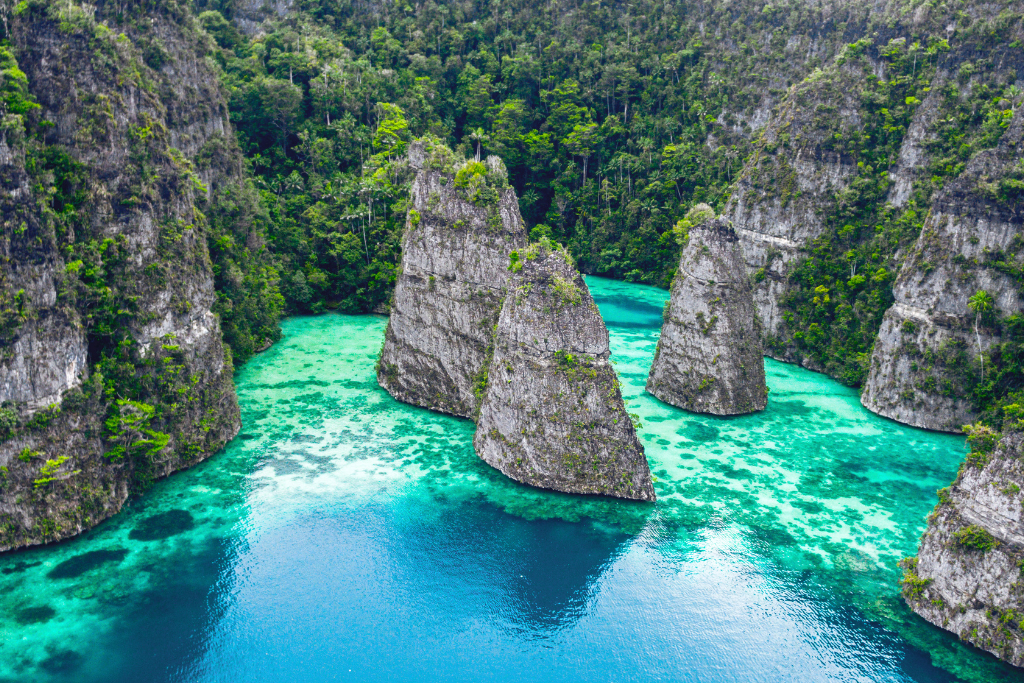 Scenic aerial view of Raja Ampat's karst islands surrounded by vibrant turquoise and deep blue waters, lush green vegetation, and dramatic limestone cliffs.