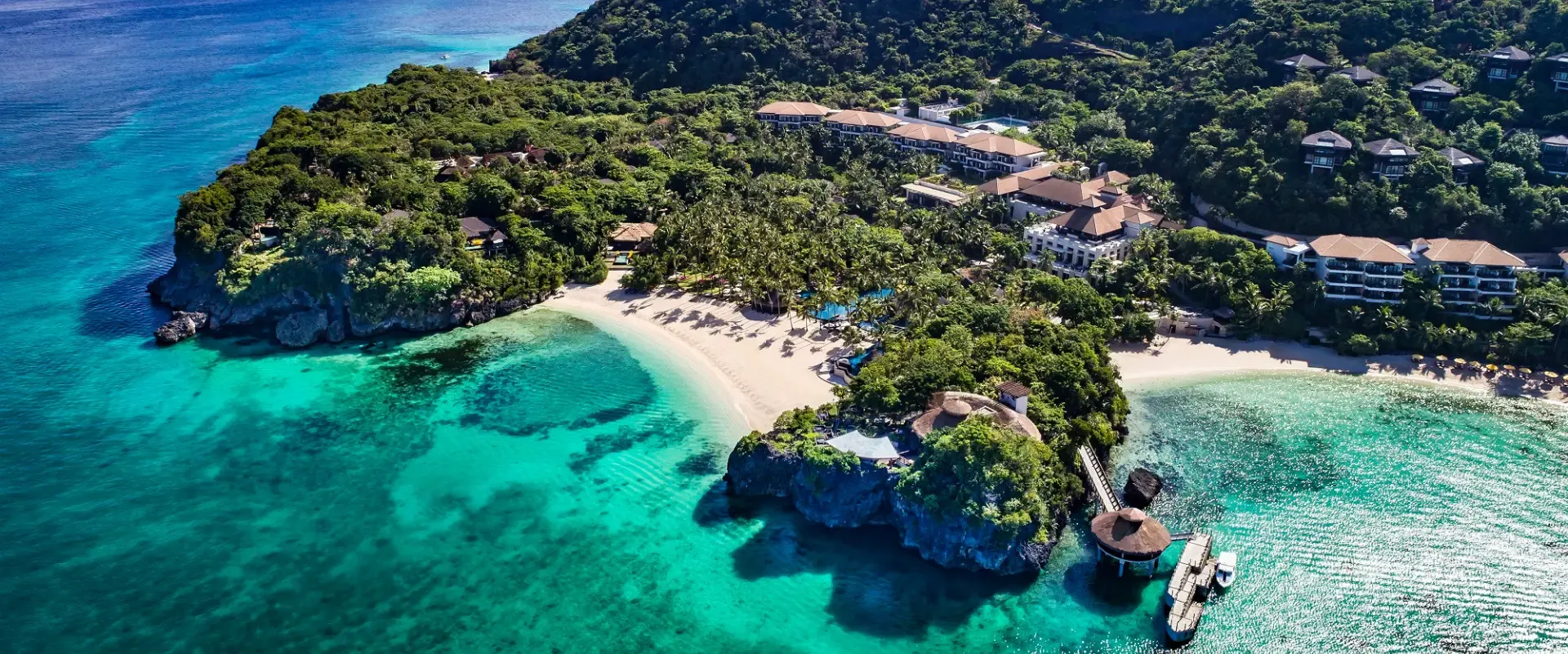 Aerial view of Shangri-La Boracay resort surrounded by lush green hills, clear turquoise waters, and a private white-sand beach.