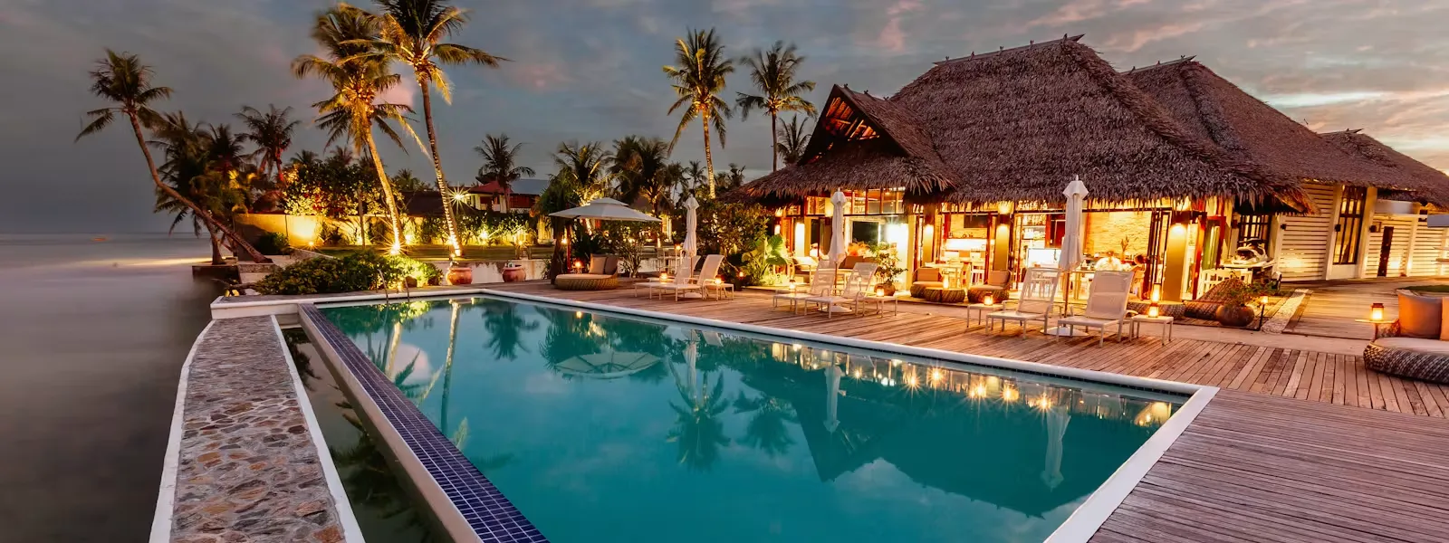Isla Cabana Resort's oceanfront pool and cabanas illuminated at dusk on General Luna beach, Siargao.