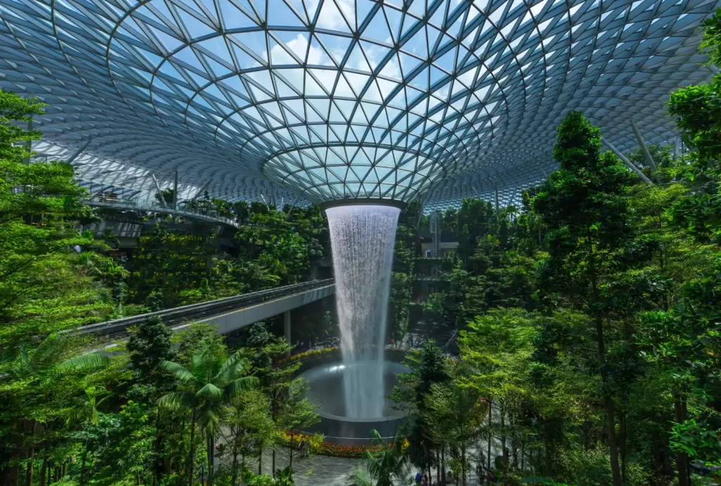 A stunning waterfall cascades through a lush tropical forest at Jewel Changi Airport, creating a serene oasis.