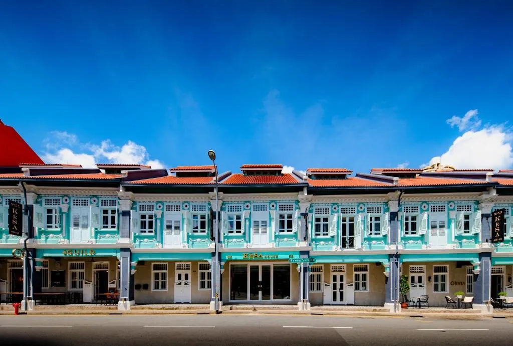 Vibrant row of historic, turquoise and white shophouses in Singapore, featuring traditional architecture and terracotta roofs under a bright blue sky. A picturesque sight for travelers on Singapore tours and a highlight of Singapore holidays offered by our Singapore tour operator.