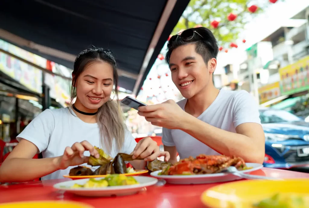 A couple enjoying a delicious meal together at a table in Singapore, surrounded by vibrant dishes and a warm atmosphere.